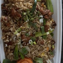 F5. Roasted Pork Fried Rice - A rectangular container holds fried rice mixed with vegetables and pieces of meat. The dish is garnished with chopped green onions and a carved carrot flower at the corner. The rice appears well-cooked with visible grains and ingredients, presented in a takeout style.