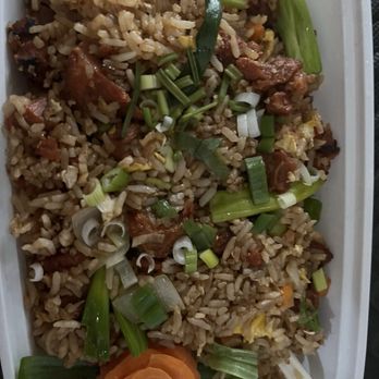 Thai Accent - F5. Roasted Pork Fried Rice - A rectangular container holds fried rice mixed with vegetables and pieces of meat. The dish is garnished with chopped green onions and a carved carrot flower at the corner. The rice appears well-cooked with visible grains and ingredients, presented in a takeout style. - Thai Near Me - West Warwick, Rhode Island