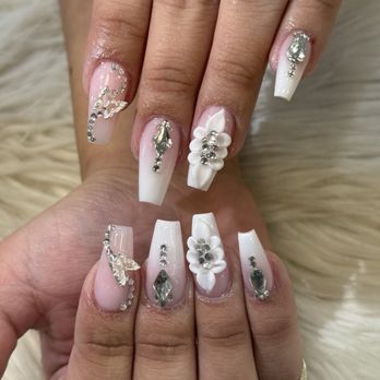 Flashy Nails - A hand displays long white acrylic nails with rhinestone embellishments, 3D floral accents, and intricate designs, set against a soft, furry background. - Nail Salons Near Me - Albuquerque, New Mexico