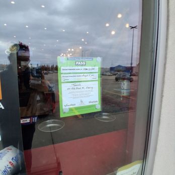 Tahini's - A pass sticker from the Durham Region Health Department is attached to a glass door, showing the inspection results as of October 21, 2023. The sticker includes the business address and inspection details. The reflection of the parking lot and cloudy sky can be seen through the glass, along with interior lighting reflections and a person taking the photo. - Mediterranean Near Me - Pickering, Ontario