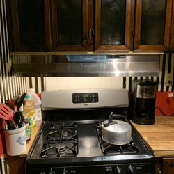 Gordon Electric Supply - 46" silver range hood, beside stove, between coffee maker, on hooks attached to range hood is hanging glass on chain. keeps grease coffee ma