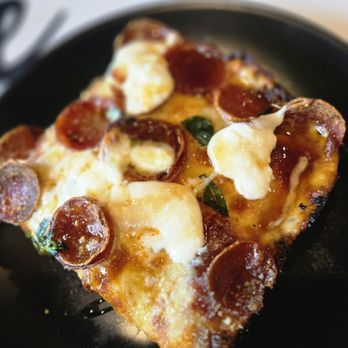 Pizzaboy - A slice of pepperoni pizza with melted cheese and pepperoni slices on a black plate, served in a restaurant setting. - Pizza Near Me - Chicago, Illinois