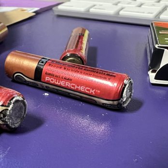 Filmtools - The date on these said good until 2025. Which means they were manufactured in 2015. Why are they selling such old stock? - Multiple used batteries with damaged or corroded ends are placed on a purple surface. A keyboard is visible in the background, along with a partially opened box containing additional batteries. The batteries are red and black, and some show signs of wear and corrosion, indicating they are no longer functional. - Photography Stores & Services Near Me - Burbank, California