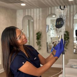 IV Elements - IV Elements staff member preparing an IV vitamin therapy bag on a stand, wearing gloves and glasses at the wellness lounge.