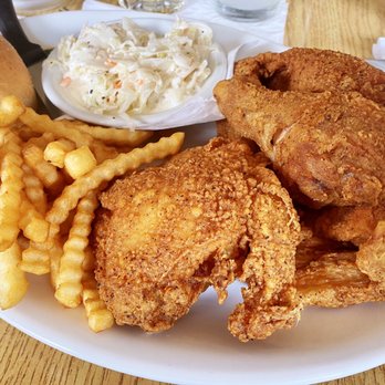 Spanky's Hideaway - Spanky's Broasted Chicken 4pc with crinkle fries - The image shows a white plate with several pieces of fried chicken, including drumsticks and thighs, alongside crinkle-cut fries. A small bowl of coleslaw with shredded cabbage and carrots in mayonnaise is also present, along with a bread roll. The setting appears to be a casual restaurant with a wooden table surface and utensils nearby. - Bars Near Me - Mequon, Wisconsin