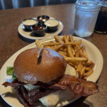 Huckleberry's - A burger with bacon, lettuce, and cheese is served with French fries and dipping sauces on a plate at a restaurant. - Breakfast & Brunch Near Me - Modesto, California