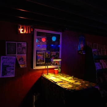 Que Sera - a dark room with a table and posters on the wall - Dive Bars Near Me - Long Beach, California Que Sera - a dark room with a table and posters on the wall - Dive Bars Near Me - Long Beach, California