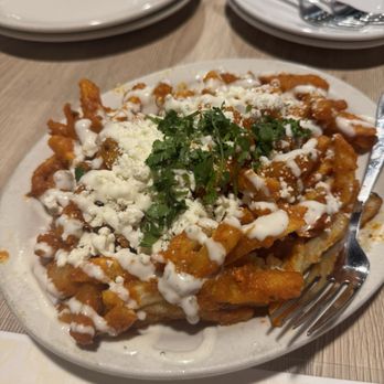 Curry Corner - Tikka Masala Fries - A dish of tikka masala fries garnished with cilantro, cheese, and drizzled with sauce, served on a white plate at a restaurant. - Pakistani Near Me - Tempe, Arizona