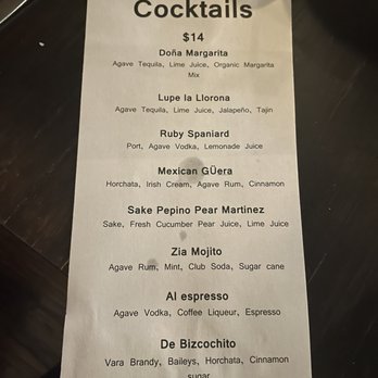 Debajo Tapas ABQ - Cocktail menu - A printed cocktail menu featuring a list of mixed drinks priced at $14, including ingredients such as agave tequila, lime juice, and various spirits. The menu is on a dark surface, with some shadows and reflections visible, and includes drinks like Doña Margarita, Lupe la Llorona, and Ruby Spaniard. - Spanish Near Me - Albuquerque, New Mexico