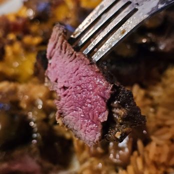 Texas Roadhouse - Close-up of a fork holding a piece of the Filet cooked medium rare, with the Fitet Medallions dish in the background. - Barbeque Near Me - Roanoke, Virginia Texas Roadhouse - Close-up of a fork holding a piece of the Filet cooked medium rare, with the Fitet Medallions dish in the background. - Barbeque Near Me - Roanoke, Virginia