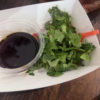 Maru Plus - From the condiment bar - A serving of mixed greens with a small cup of soy sauce on a wooden table, likely at a Japanese restaurant. - Japanese Near Me - Tucson, Arizona