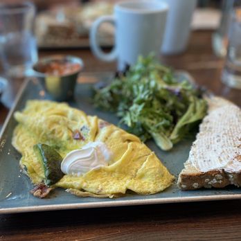 First Watch - Bacado omelette - A breakfast plate featuring a folded omelette with vegetables, a side salad, and a slice of bread with spread, served on a rectangular ceramic plate. - Cafes Near Me - Tucson, Arizona