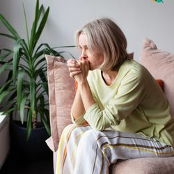 Connections Wellness Group - A woman sitting on a couch with her hands clasped and looking thoughtful or concerned, representing contemplation or emotiona...