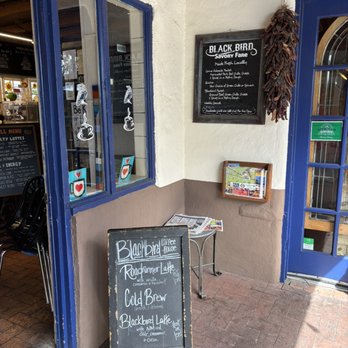 Blackbird Coffee House - signange - Outside Blackbird Coffee House, a chalkboard menu displays drinks like the Roadrunner Latte and Cold Brew, with a chili pepper decoration hanging nearby. - Coffee & Tea Near Me - Albuquerque, New Mexico