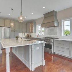 AMC Kitchen & Bath - This elegant kitchen showcases light grey cabinetry, marble countertops, and a large central island with decorative legs...