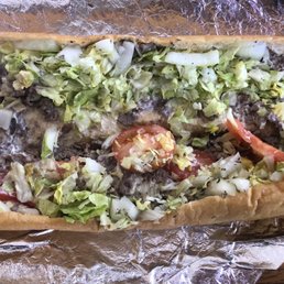 Chicken Cheese Steaks - A cheesesteak hoagie with shredded lettuce, sliced tomatoes, and cooked beef in a long sandwich bun, served on aluminum foil.