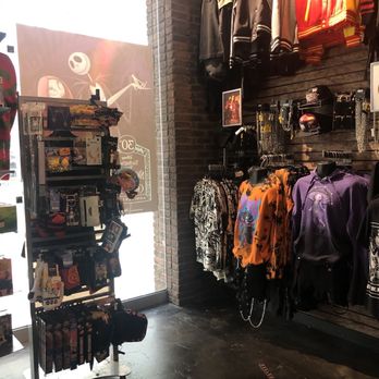 Hot Topic - Inside a retail store, clothing items such as jackets, hoodies, and shirts are displayed on racks and hangers against a brick wall. Accessories like jewelry and hats are also visible. - Accessories Near Me - Burbank, California