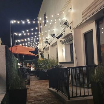 Morse Code Lounge - Nighttime outdoor patio with string lights, an orange umbrella, and seating areas, likely part of a restaurant or lounge. - Wine Bars Near Me - Winter Park, Florida