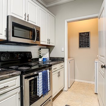 Elevate 155 - Kitchens featuring black-fusion counter tops, white cabinetry, stainless steel appliances, and a laundry room. - Apartments Near Me - Mount Dora, Florida Elevate 155 - Kitchens featuring black-fusion counter tops, white cabinetry, stainless steel appliances, and a laundry room. - Apartments Near Me - Mount Dora, Florida