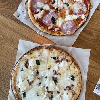 Blaze Pizza - Two build your own pizzas with white sauce and the classic red sauce - Two pizzas are shown on a wooden table, each on a piece of parchment paper. The top pizza has pepperoni, cheese, and basil, while the bottom pizza appears to be a cheese pizza with some additional toppings. Both pizzas have a golden-brown crust and are cut into slices. - Fast Food Near Me - Orem, Utah