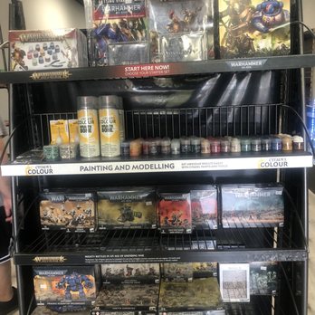 Clovis Cards & Comix - Gear inside 6/24/23 - A black metal shelving unit in a gaming store holds Warhammer miniatures, paints, and starter sets, with labels for painting and modeling supplies. - Tabletop Games Near Me - Clovis, California