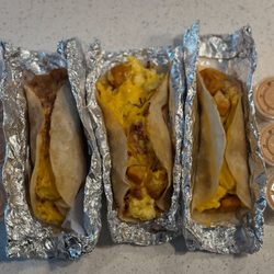 Taco Joint - One potato, bacon, egg, and cheese in the middle and two  potato bean and cheese breakfast tacos with chipotle sauce on the side.