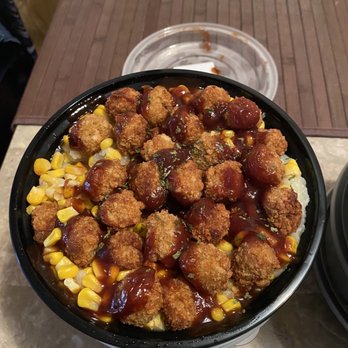 GreenBites - Mashed Potato Bowl delicious!!! - A bowl containing a vegan mashed potato dish topped with crispy, breaded bites and drizzled with a dark sauce. The bowl also includes corn and other vegetables, presented on a table with a brown placemat and a clear plastic lid in the background. - Vegan Near Me - Chicago, Illinois