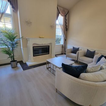 Everclean Services - Formal livingroom spotless and windows wiped down very well. - A living room features a white fireplace, two large windows with curtains, and beige sofas with decorative pillows, creating a cozy space. - Home Cleaning Near Me - Pasadena, California