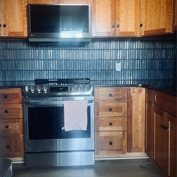 López Construction - Kitchen backsplash tile - The kitchen features wooden cabinetry, a stainless steel LG oven with a towel hanging on the handle, and a mounted television above the cabinets. - Masonry/Concrete Near Me