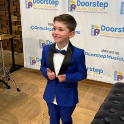 Doorstep Music Lessons - Student appears in blue tuxedo in front of backdrop