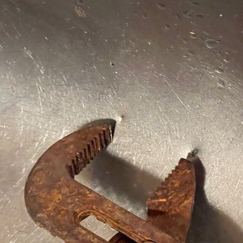 Pipeworks Services - channel lock points align with sink punctures. - The image features a rusty pipe wrench positioned on a metallic surface. The wrench exhibits significant rust and corrosion, with visible wear on its teeth and handle. The surface beneath is metallic, with a slightly textured appearance and some minor scratches or marks. The lighting highlights the rusted texture of the wrench, emphasizing its aged condition. - Heating & Air Conditioning/HVAC Near Me - Gaithersburg, Maryland