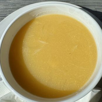 Deolinda's Artisans - Onion soup - A white bowl contains onion soup with a transparent, yellowish broth, placed on a table with a textured placemat. - Portuguese Near Me - Danbury, Connecticut