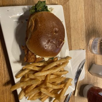 Apache Trout Grill - See what I wrote - A fried chicken sandwich with lettuce and sauce on a bun, served with French fries on a rectangular white plate. - New American Near Me - Traverse City, Michigan