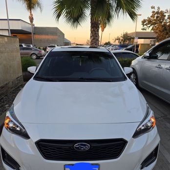 Ceramic Garage - A white Subaru sedan is parked in a parking lot with palm trees and other cars visible in the background during sunset. - Car Window Tinting Near Me - Modesto, California