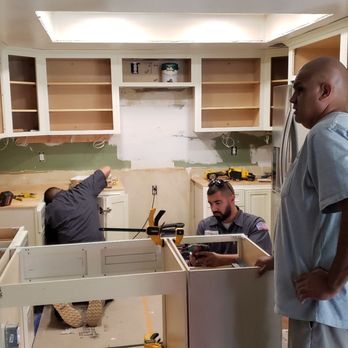 Cova Construction - Cabinets getting there - Three workers are installing kitchen cabinets in a kitchen under renovation, with open shelves and tools visible. - General Contractors Near Me - Corona, California