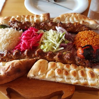 Meat Point - Beautiful presentation and delicious! - A wooden serving board displays a selection of Middle Eastern cuisine, including rice, shredded salad, grilled meat skewers, flatbread, and roasted vegetables. The dishes are arranged with colorful vegetables and various textures, served on a table with water glasses and a white plate in the background. - Turkish Near Me - Toronto, Ontario