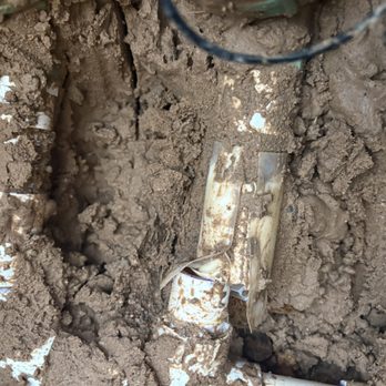 Alberto's Landscaping - Before - broken pipe for irrigation system - A broken irrigation pipe is partially buried in soil, with dirt and soil surrounding it, indicating a plumbing issue in an outdoor area. - Tree Services Near Me