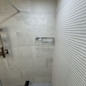 Porcelanosa - A shower corner with large light gray tiles on the wall, a textured white wall, and a metal towel rack. - Kitchen & Bath Near Me - Paramus, New Jersey
