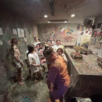 Art Barn ATX - Children getting into the splatter with Amber coaching on.... - Children with paint on their clothes and skin gather around an instructor in a paint-splattered art studio, celebrating a birthday. - Art Classes Near Me - Leander, Texas