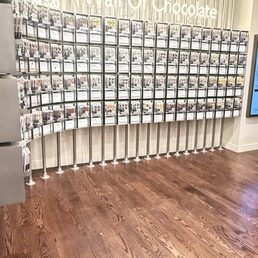 A wall of chocolate - A display wall with numerous chocolate items arranged in a grid, labeled 'Wall of Chocolate,' in a retail store setting.