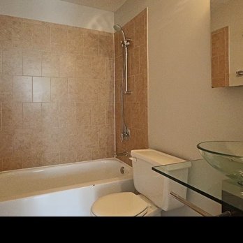 Roman Remodeling - A bathroom features a bathtub with beige tile surround, a white toilet, and a glass vessel sink on a black countertop. - General Contractors Near Me - Chicago, Illinois