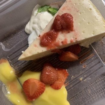 Loon Lodge - Cheesecake with lemon sauce to go - A slice of cheesecake with strawberry topping is placed on a clear tray, accompanied by fresh strawberries and a dollop of cream with a mint leaf. - Bed & Breakfast Near Me - Rangeley, Maine