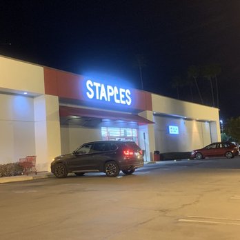 Staples - The image depicts a Staples store in a parking lot at night. The store has a brightly lit sign reading 'STAPLES' above the entrance. There are a few parked cars in front of the store, and the parking lot appears mostly empty. The sky is dark, and the area is illuminated by store and parking lot lights, with some palm trees visible in the background. - Printing Services Near Me - Studio City, California