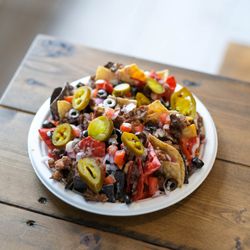 The Bend - Our Ultimate Nachos - Corn tortilla chips, jalapeno, onion, tomato, olives, house-made cheese sauce, and white bbq sauce.