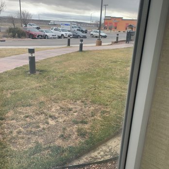 Applebee's Grill + Bar - It is right by our hotel. - A parking lot with several cars and a street with moving vehicles are visible through a window on a cloudy day. - American Near Me - Gallup, New Mexico