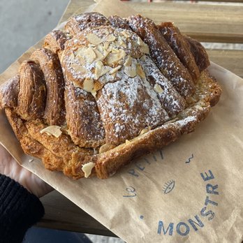 Le Petit Monstre - Croissant Almond - A rectangular pastry with a flaky crust, topped with sliced almonds, powdered sugar, and dusted with flour, placed on parchment paper. - Patisserie/Cake Shop Near Me - Brooklyn, New York