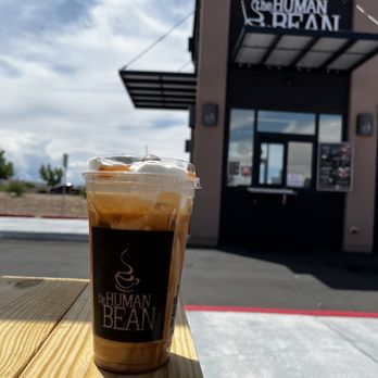 The Human Bean - A plastic cup with a coffee beverage topped with whipped cream is set on a wooden table outside a drive-thru coffee stand named The Human Bean. - Coffee & Tea Near Me - Albuquerque, New Mexico