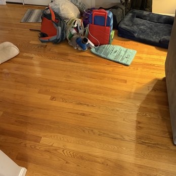 H H Flooring - A hardwood floor in a living room area is shown with various bags, a toy, and a pet bed placed on it. - Flooring Near Me - Boston, Massachusetts