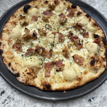 White Pie - A pizza featuring cheese, bacon, and various toppings on a black tray, served on a marble table at a restaurant. - Pizza Near Me - Denver, Colorado