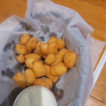 Jersey's Bar & Grill - Half eaten cheese curd appetizer. Sorry forgot to take the picture before we dug in. - Fried cheese curds served in a basket lined with parchment paper, accompanied by a cup of ranch dressing, on a wooden table at a casual dining restaurant. - American Near Me - Beloit, Wisconsin
